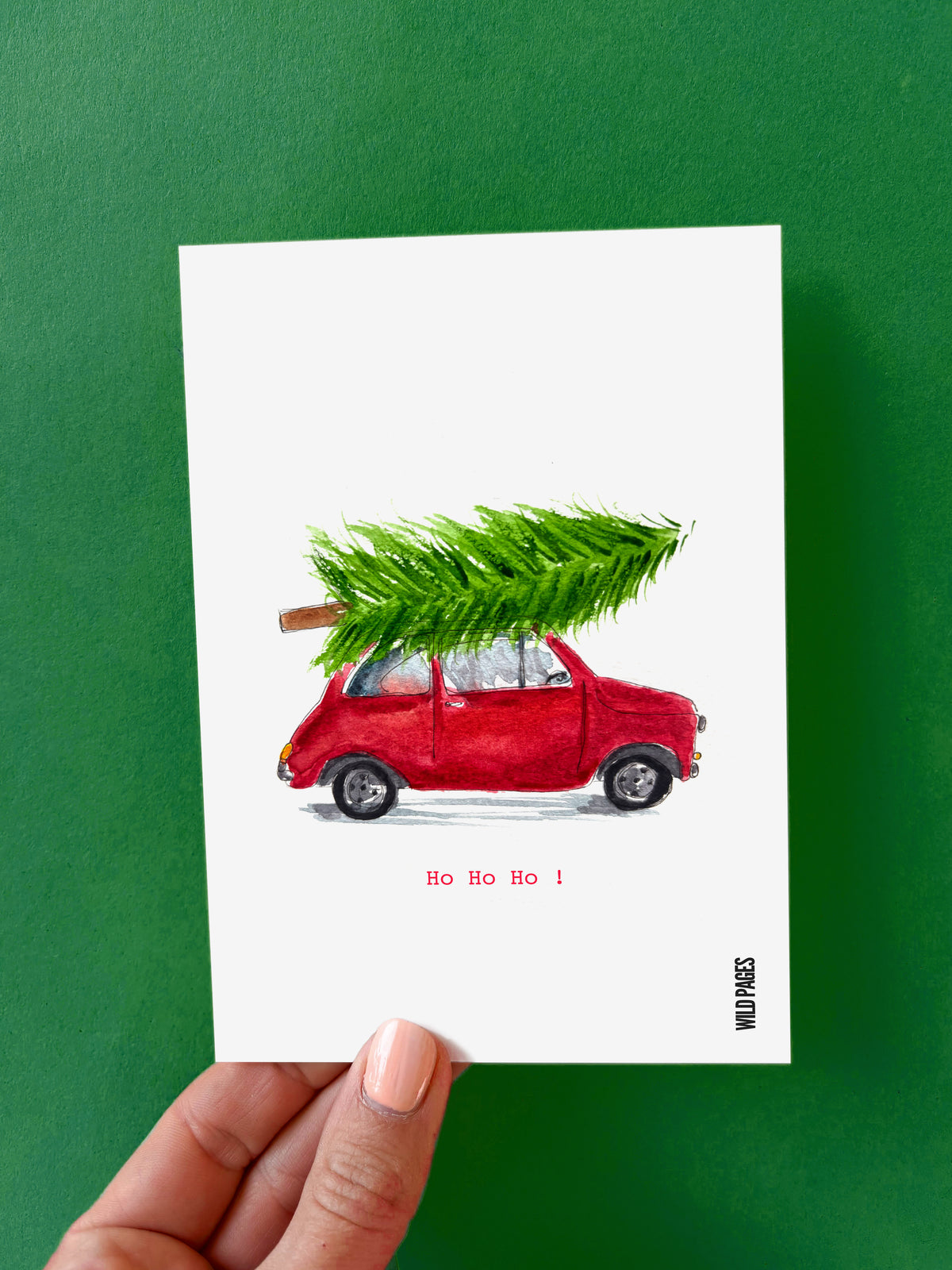 Illustration aquarelle d'une Fiat rouge portant un sapin sur son toit, texte « Ho Ho Ho ! », carte tenue devant un fond vert.