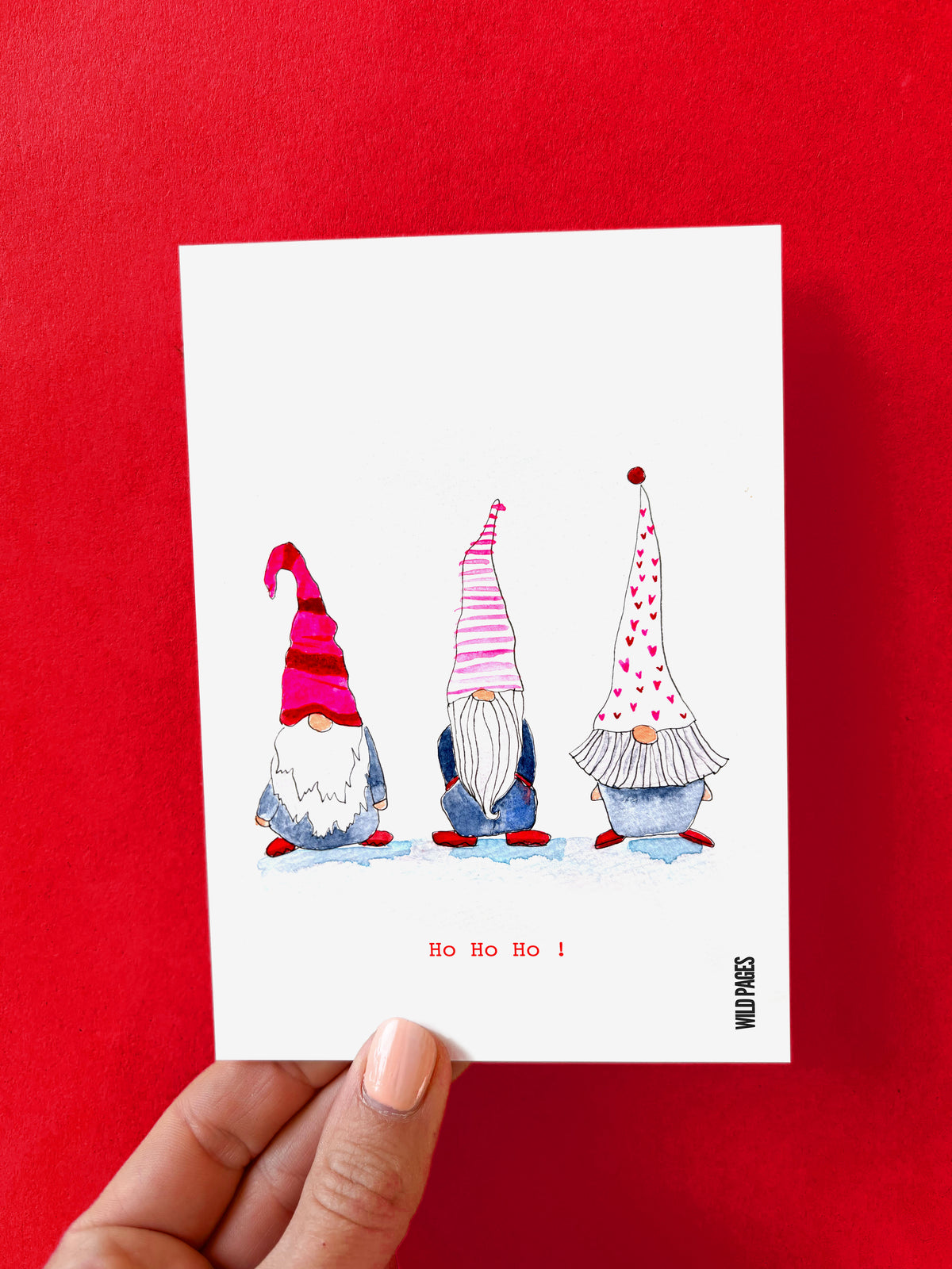 Illustration aquarelle de trois lutins de dos avec des bonnets roses et rouges, texte « Ho Ho Ho ! », carte tenue devant un fond rouge.